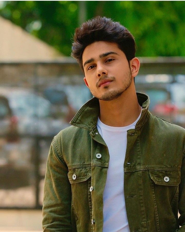 Man wearing a green jacket over a white shirt with a blurred outdoor background